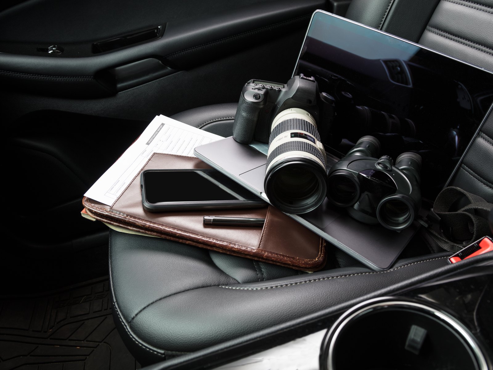 Camera, binoculars, and notebook on the seat of an investigator's vehicle